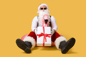 Santa Claus with gift on swim ring against yellow background. Christmas in July