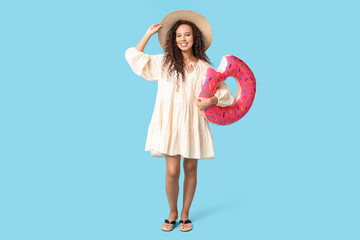 Beautiful young African-American woman with inflatable ring on blue background