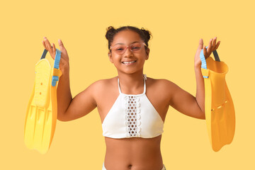 Happy African-American girl with flippers on yellow background