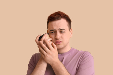Young man with cup of coffee suffering from tooth ache on beige background