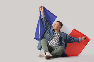 Young man with flag of France sitting on grey background