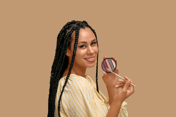 Young African-American woman with braids and beautiful makeup holding palette of eyeshadows and...