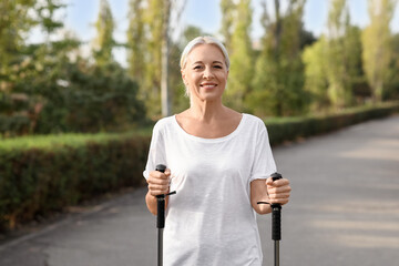 Beautiful mature happy woman training with walking poles in park