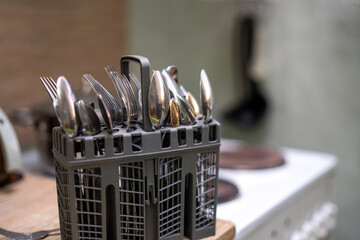 collection of stainless steel forks and spoons neatly arranged in a dishwasher utensil container,...