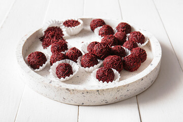 Plate with delicious chocolate truffles and paper cups on white wooden background