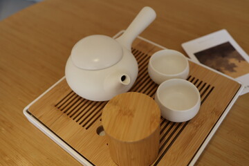 White teapot and cups arranged on a wooden tray.