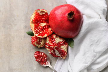 Fresh ripe pomegranates and spoon with seeds on grey background