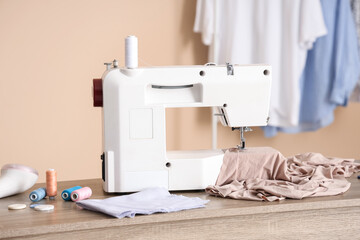 Modern sewing machine with beige fabric and tailor's supplies on table in atelier