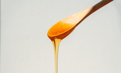 natural honey falling from a wooden spoon on a white background