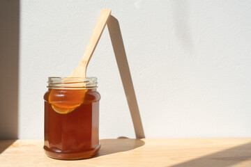 glass jar of honey with a wooden spoon inside the jar, on a white background