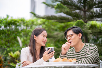 Happy Asian couple enjoy spending time together at backyard at home, People have have conversation outdoor. Healthy life and insurance concept. Marriage drink coffee in garden.