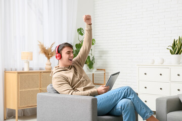 Handsome young man with headphones and tablet computer sitting on armchair at home