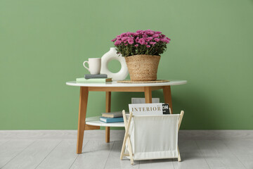 Wicker basket with chrysanthemum flowers, books and magazines on coffee table against green background