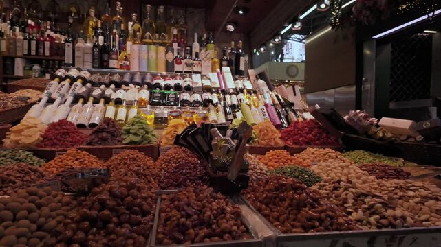 A gourmet food stall at Mercat de la Boqueria in Barcelona, showcasing a selection of nuts, dried fruits, specialty snacks, and bottles of olive oil and wine. A market full of Mediterranean flavors