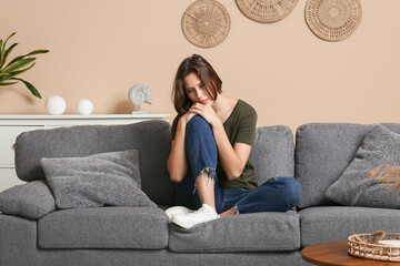 Depressed young woman sitting on sofa in living room