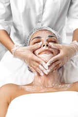 Cosmetologist applying cream on female face in cosmetology salon.