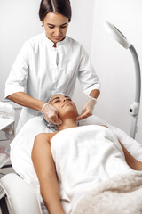 Obraz premium Cosmetologist applying cream on female face in cosmetology salon.