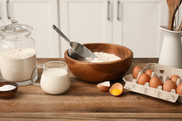 Flour in jar with eggs, bowl, scoop and jug of milk for preparing dough on kitchen counter