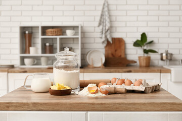 Flour in jar with eggs, jug of milk, scoop and butter for preparing dough on kitchen counter