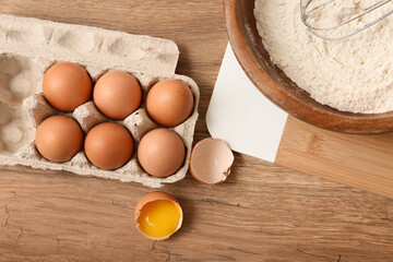 Bowl of flour with eggs for preparing dough on wooden background