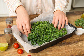 Woman with baking dish of fresh kale cabbage leaves and tomatoes in kitchen