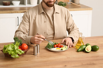 Man eating tasty fried egg, kale cabbage, avocado and tomatoes at wooden table