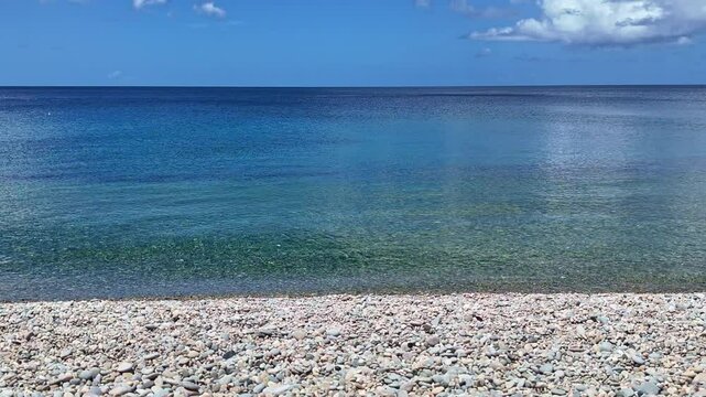 Calm crystal-clear sea meets a peaceful pebble beach under tropical blue skies. A relaxing travel background, ideal as copy space for advertising or vacation b-roll.