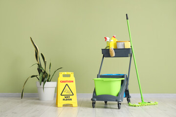 Trolley with cleaning supplies and  caution sign near green wall
