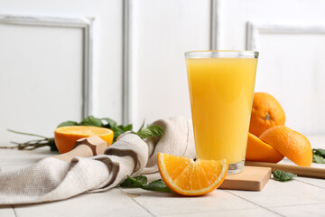 Glass of tasty juice with oranges, mint leaves and wooden juicer on white tile table