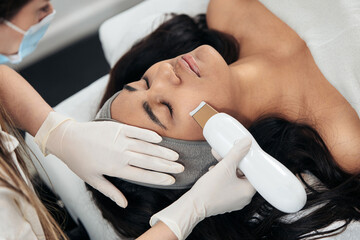 The beautician at the salon performs a facial cleansing treatment for a young female client using specialized equipment