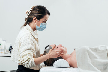 Master giving facial massage to young woman in massage parlor