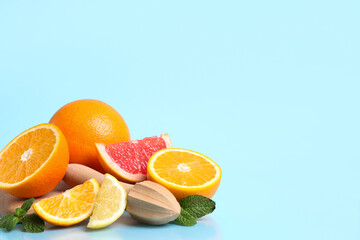 Wooden board with different cut citrus fruits, juicer and mint leaves on blue background