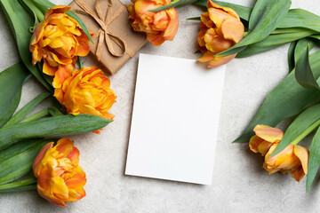 Blank greeting card mockup with gift box and tulips flowers over grey stylish background, top view with copy space