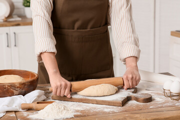 Woman rolling out fresh dough in kitchen