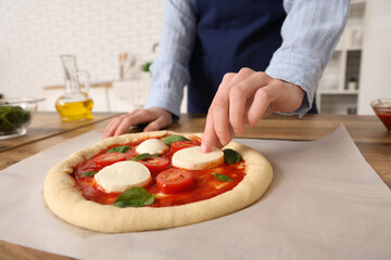 Woman putting mozzarella cheese on dough for pizza near table in kitchen