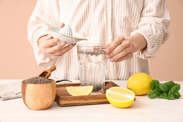 Woman adding lemon juice into glass of water with chia seeds near table
