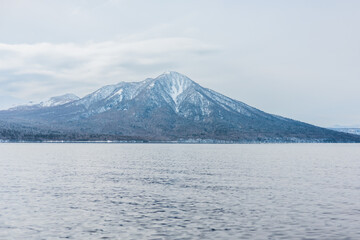 Majestic snow covered mountain peak with calm lake reflection ; lake Shikotsu japan