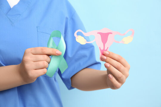 Female doctor holding turquoise ribbon with paper uterus on blue background, closeup. Cervical Health Awareness Month