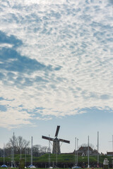 Windmill stands proudly at sunset near the harbor with moored boats under a cloudy sky in a tranquil coastal setting
