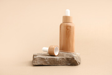 Decorative stone and bottle with cosmetic product on beige background