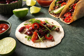 Fresh tasty tacos and ingredients on green marble tray as background