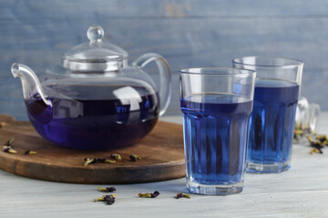Glasses and teapot of butterfly pea flower tea on blue wooden background