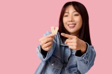 Pretty young Asian woman pointing at chewing gums on pink background