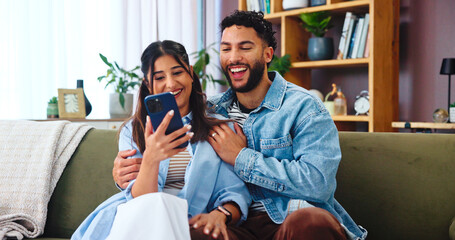 Couple, smartphone and laugh on sofa with hug, social media and funny gossip story in home. Woman,...
