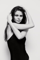 Fototapeta premium Elegant woman with long hair posing gracefully in a black bodysuit, showcasing confidence and poise against a soft white background. Fashion and beauty concept.