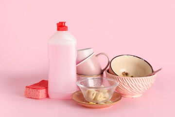 Dirty dishes, detergent and sponge on pink background