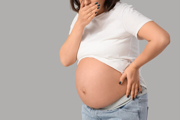 Pregnant woman suffering from toxicosis on grey background