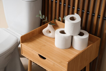 Rolls of toilet paper and vase on table near folding screen in bathroom