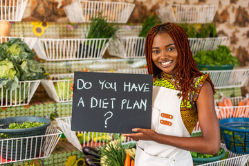 African woman small business owner holding diet plan signage at her fresh produce fruits and...