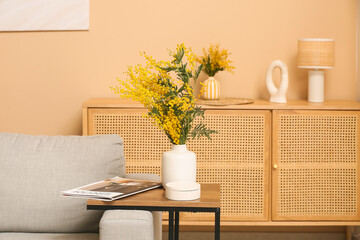 Vase with mimosa flowers and magazine on table in living room